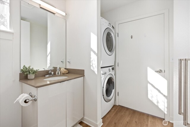 laundry area with laundry area, stacked washing maching and dryer, light wood-style floors, and a sink