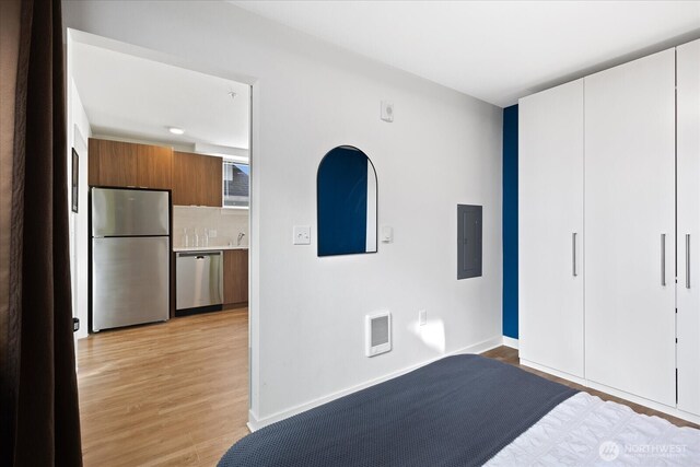 unfurnished bedroom featuring visible vents, light wood-style flooring, electric panel, freestanding refrigerator, and baseboards