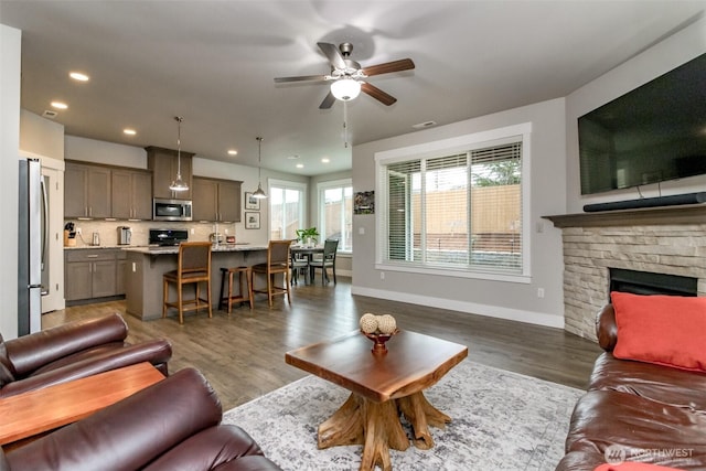 living area featuring a ceiling fan, wood finished floors, recessed lighting, a stone fireplace, and baseboards