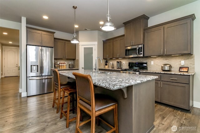 kitchen featuring dark brown cabinetry, light stone counters, wood finished floors, stainless steel appliances, and a sink