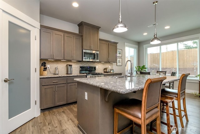 kitchen featuring a sink, stainless steel appliances, light wood-type flooring, and backsplash