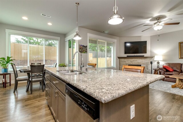 kitchen featuring visible vents, light stone countertops, dishwasher, light wood-type flooring, and a sink