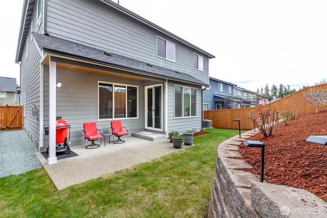 rear view of property featuring central AC unit, a fenced backyard, a shingled roof, a patio area, and a lawn