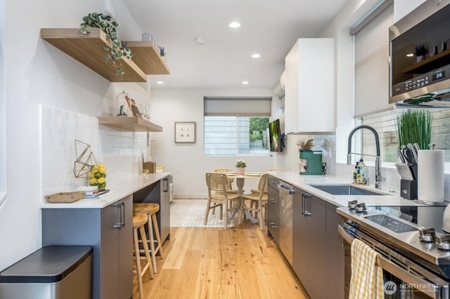 kitchen featuring open shelves, light countertops, appliances with stainless steel finishes, light wood-style floors, and a sink