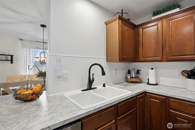 kitchen featuring a chandelier, brown cabinetry, light countertops, and a sink