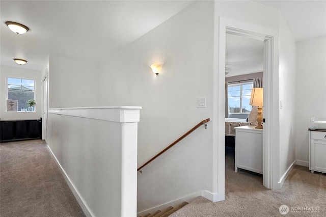 hallway with an upstairs landing, light colored carpet, and baseboards