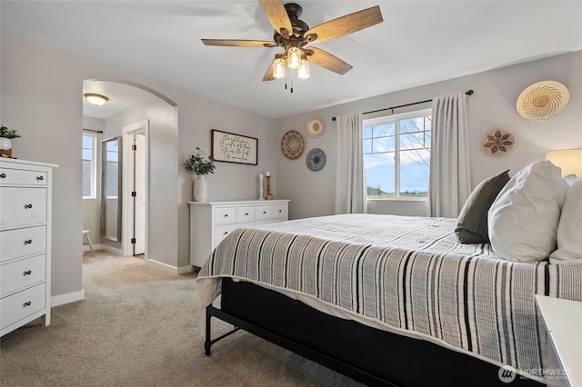 bedroom with a ceiling fan, baseboards, arched walkways, and light carpet