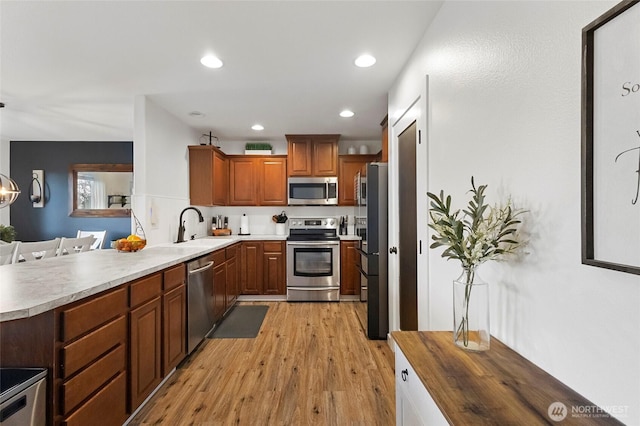 kitchen featuring light wood finished floors, a peninsula, recessed lighting, a sink, and stainless steel appliances