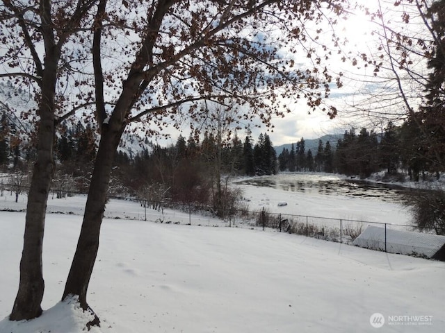 snowy yard with a view of trees and fence