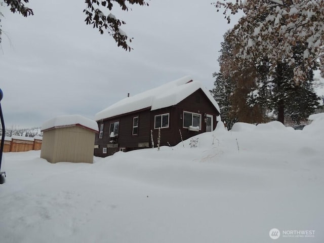 snow covered property with an outbuilding, fence, and a shed