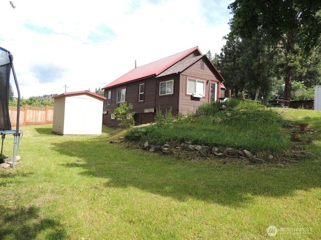 view of home's exterior featuring a trampoline, fence, a yard, an outdoor structure, and a storage unit