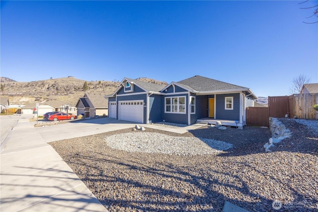 view of front of house with roof with shingles, an attached garage, fence, a mountain view, and driveway