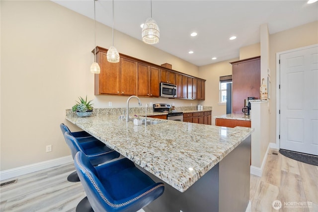 kitchen with a peninsula, light stone counters, stainless steel appliances, and a sink