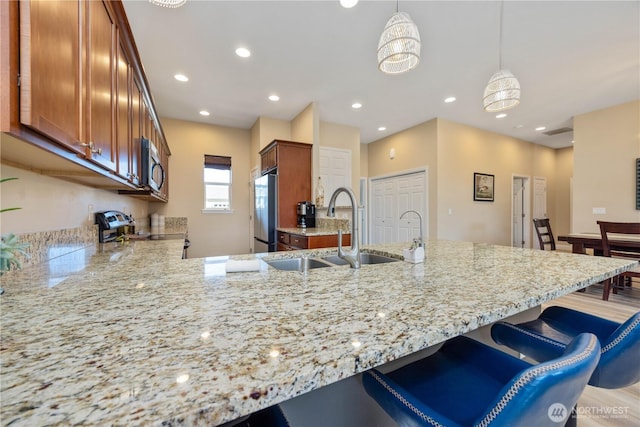 kitchen with a peninsula, a sink, a kitchen breakfast bar, appliances with stainless steel finishes, and light stone countertops