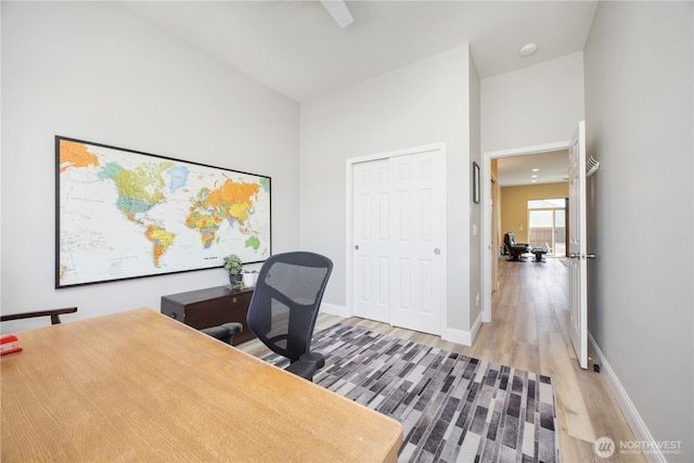 office area featuring light wood-type flooring, a high ceiling, and baseboards