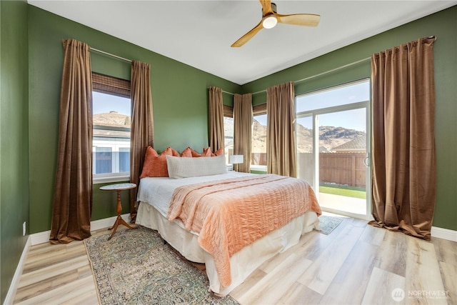 bedroom featuring access to outside, multiple windows, a mountain view, and light wood-style floors