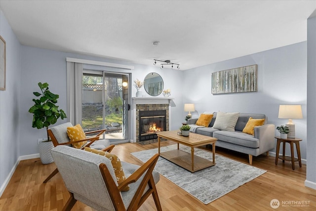 living area with rail lighting, a brick fireplace, baseboards, and light wood finished floors