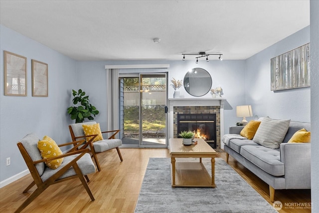 living room featuring a fireplace, baseboards, track lighting, and wood finished floors