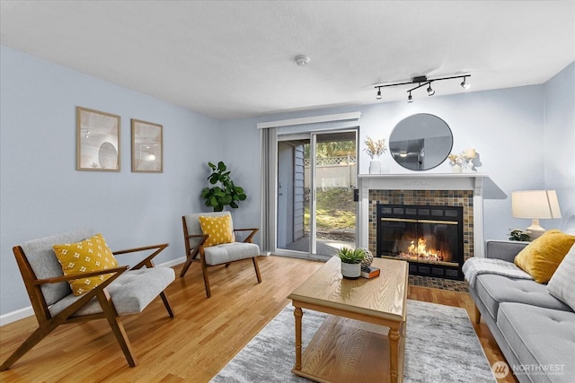 living room featuring rail lighting, baseboards, a tiled fireplace, and wood finished floors