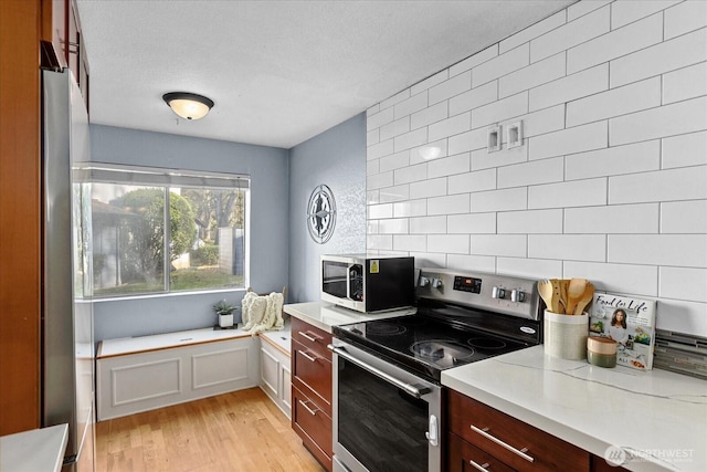 kitchen featuring a textured ceiling, stainless steel electric range, backsplash, and light wood-style floors