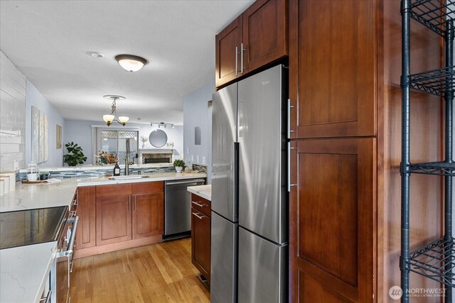 kitchen with stainless steel appliances, a sink, light wood finished floors, decorative light fixtures, and an inviting chandelier