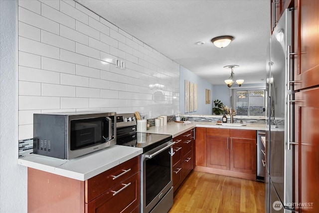 kitchen featuring light wood finished floors, decorative backsplash, stainless steel appliances, light countertops, and a sink