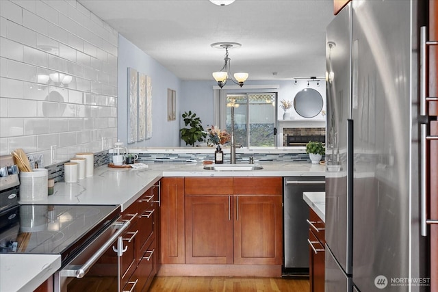 kitchen with brown cabinets, stainless steel appliances, decorative backsplash, a sink, and light stone countertops