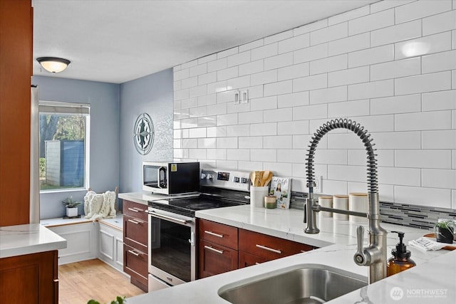 kitchen with light wood-style floors, appliances with stainless steel finishes, light stone counters, and backsplash