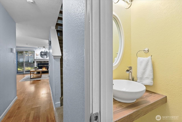 bathroom featuring baseboards, a textured wall, wood finished floors, a lit fireplace, and a sink