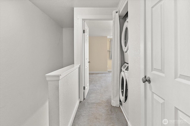 washroom featuring laundry area, baseboards, stacked washer / drying machine, and light colored carpet