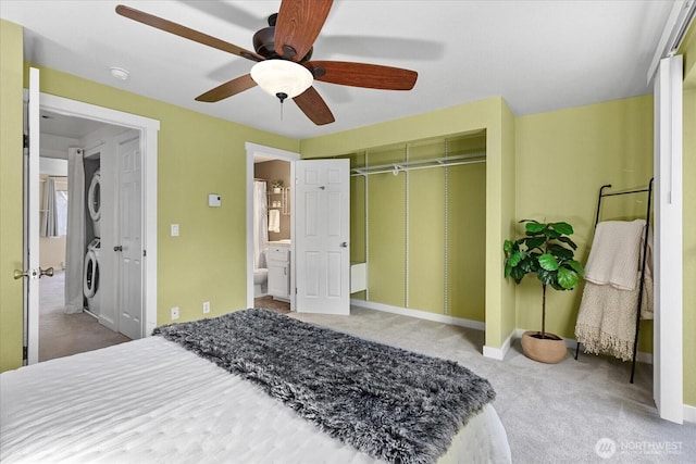 carpeted bedroom featuring a closet, stacked washer and clothes dryer, ceiling fan, and baseboards