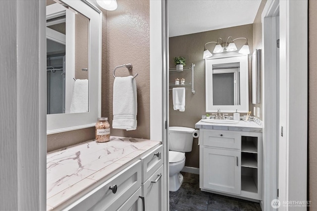 bathroom featuring toilet, a textured wall, baseboards, and vanity