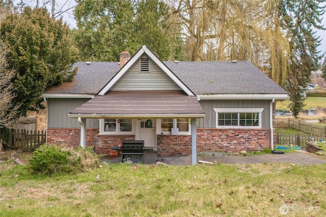 view of front of property featuring fence, a shingled roof, a chimney, a front lawn, and brick siding