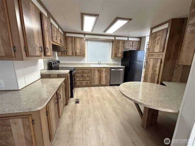 kitchen featuring light wood finished floors, a sink, stainless steel appliances, under cabinet range hood, and brown cabinets