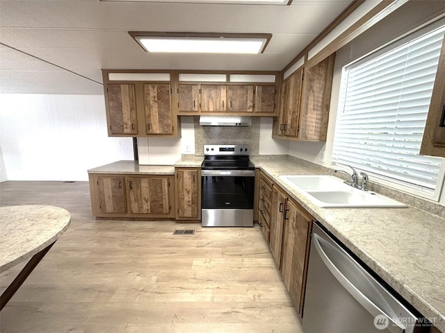 kitchen with a sink, stainless steel appliances, brown cabinets, and under cabinet range hood