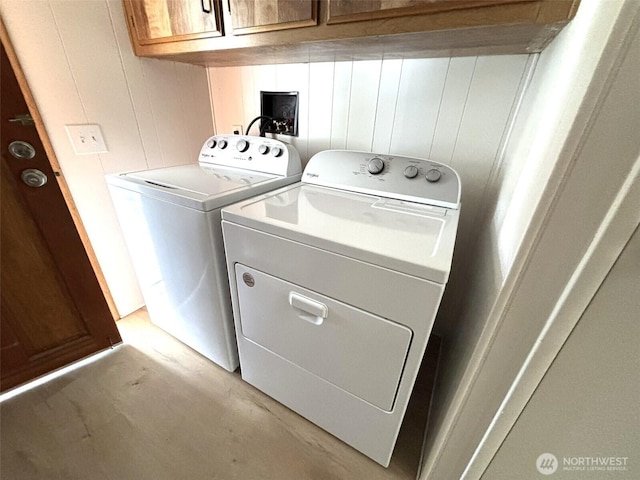 laundry area with cabinet space, wooden walls, and washer and clothes dryer