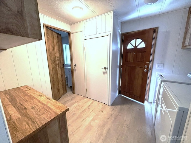 foyer entrance featuring wooden walls, washing machine and dryer, and light wood-style flooring