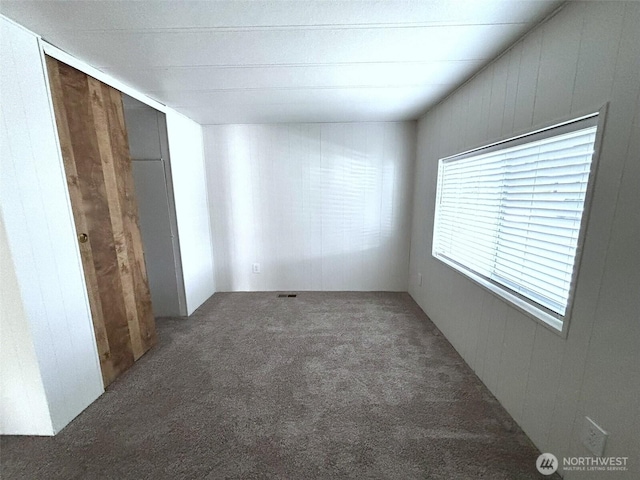 unfurnished bedroom with wooden walls and carpet flooring