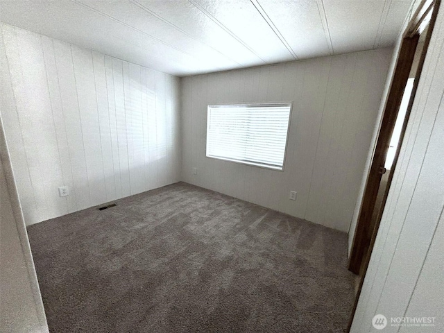 spare room with carpet, visible vents, and wood walls