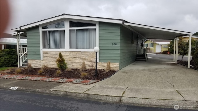 view of side of property featuring entry steps, a carport, stone siding, and driveway