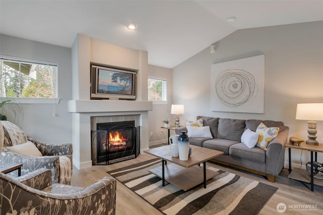 living area with light wood-style floors, a fireplace, vaulted ceiling, and baseboards