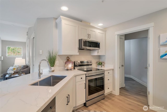 kitchen featuring recessed lighting, stainless steel appliances, a sink, white cabinets, and light stone countertops