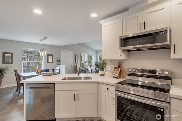 kitchen with stainless steel appliances, a peninsula, a sink, white cabinetry, and light countertops