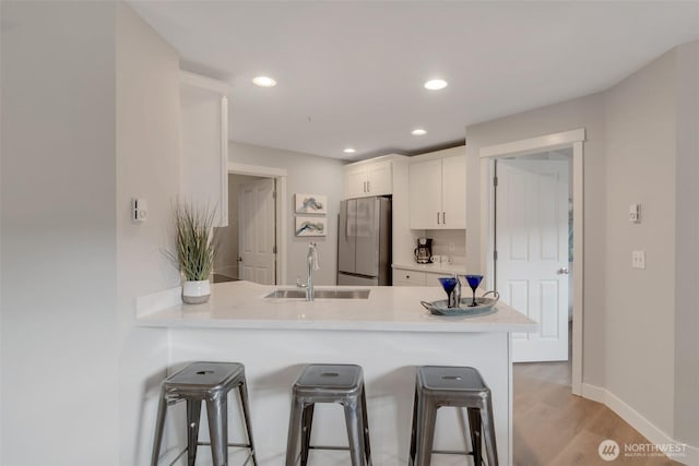 kitchen featuring light countertops, freestanding refrigerator, white cabinetry, a sink, and a kitchen bar