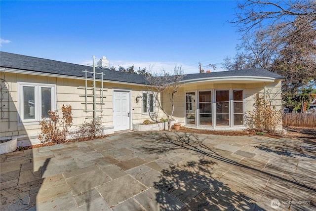 rear view of house featuring a patio, roof with shingles, and fence