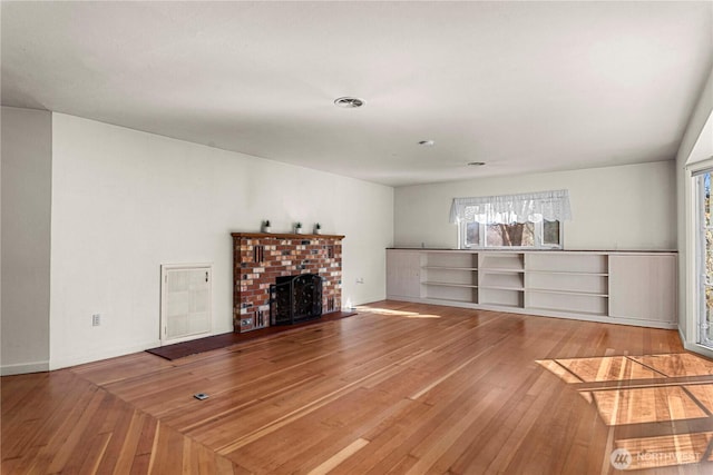 unfurnished living room with visible vents, wood-type flooring, a wealth of natural light, and a brick fireplace