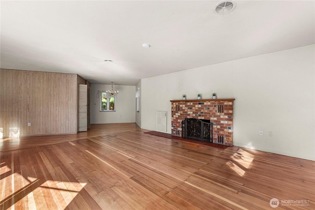 unfurnished living room with a notable chandelier, wooden walls, a fireplace, visible vents, and light wood-style floors