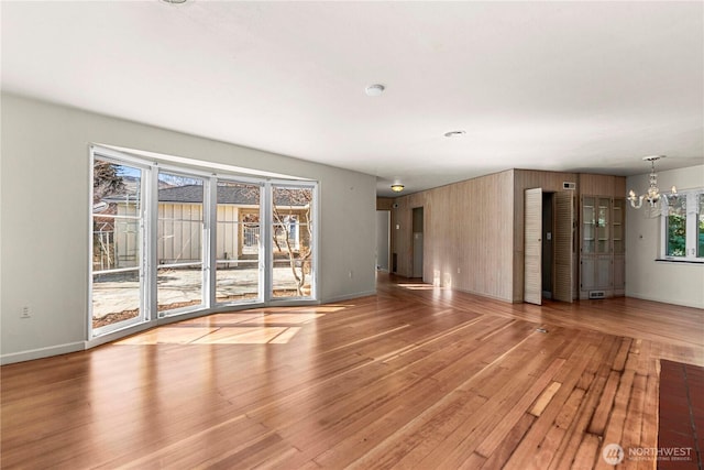 unfurnished living room featuring hardwood / wood-style flooring, baseboards, and an inviting chandelier