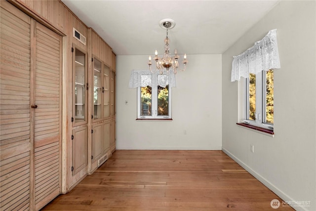 unfurnished dining area featuring light wood finished floors, baseboards, visible vents, and a chandelier