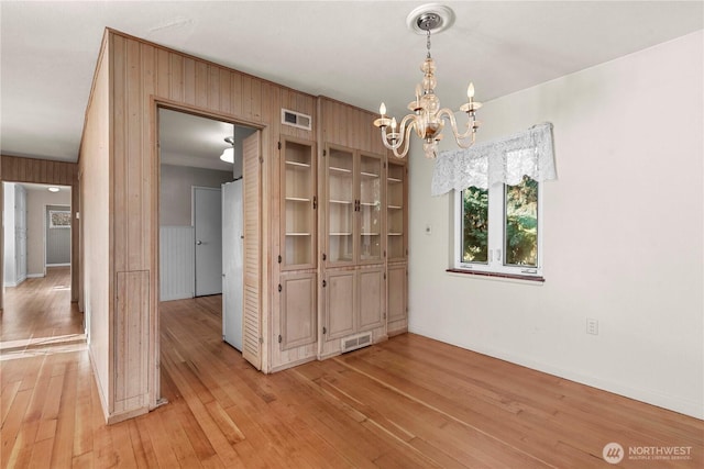 unfurnished dining area with light wood-type flooring, wood walls, visible vents, and an inviting chandelier